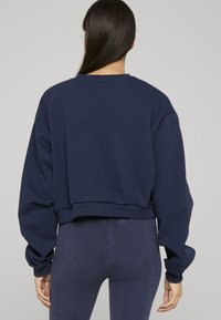 Marineblå cropped genser med rund hals, oversized ermer og ribbestrikkede mansjetter, laget av mykt bomullsmateriale. Har et ensfarget design.