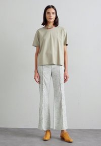 Olijfgroene korte mouwen shirt, met bloemenpatroon, uitlopende lichte broek en bruine leren schoenen. Eenvoudige, casual outfit met neutrale tinten.