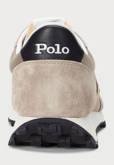 Baskets en daim beige avec talon en cuir noir. Comprend un col rembourré, une semelle intermédiaire blanche et une semelle extérieure en caoutchouc noir texturé avec un motif d'adhérence.