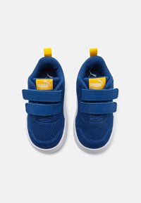 Zapatillas de malla azules con suelas blancas, dos cintas de Velcro y acentos amarillos. Logo de Puma en la lengua y en el lazo trasero. Diseño ligero.