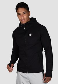 Schwarze Zip-Hoodie mit leichtem, glattem Material, ausgestattet mit einem Logo auf der Brust, taillierter Passform und Daumenlöchern an den Bündchen.