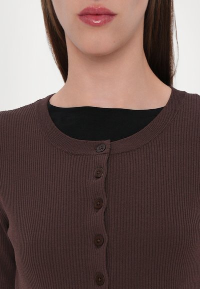 Cardigan brun à côtes avec un col rond et six boutons marron foncé. En dessous, un haut noir est partiellement visible.