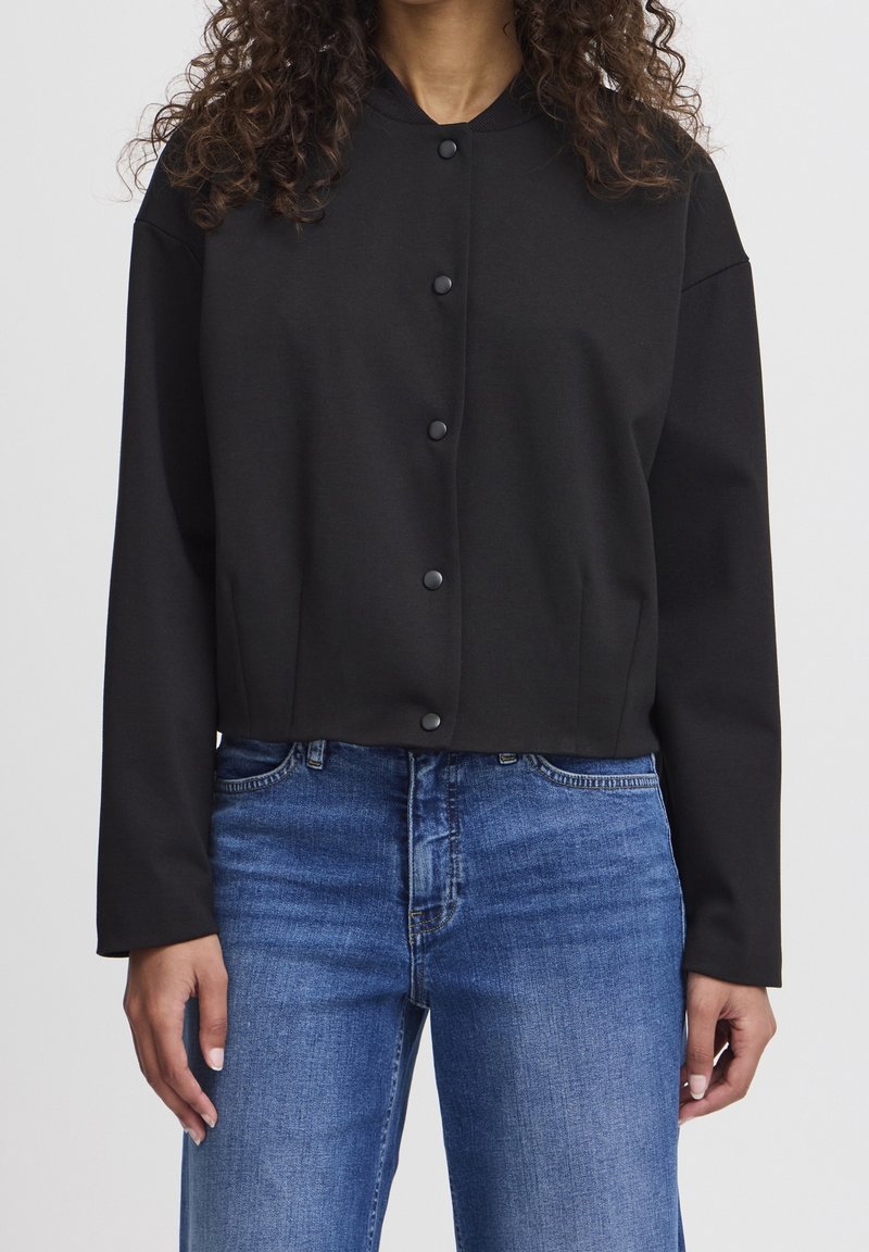 Czarna krótka kurtka zapinana na guziki, z prążkowanym kołnierzem i długimi rękawami, połączona z niebieskimi dżinsami.