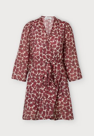 Femme debout face à l'avant portant une robe portefeuille rouge à fleurs avec des manches 3/4 et des bottes en cuir noires montantes jusqu'au genou sur un fond uni.