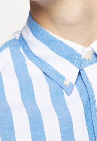 Světle modrá a bílá pruhovaná košile s límečkem a zapínáním na knoflíky, s jemnou texturou látky a klasickým límečkem.