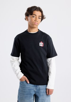 Zwarte korte mouwen t-shirt met een ronde hals, voorzien van een kleurrijke logo patch op de linkerborst. Draagt over een wit langemouwen shirt.