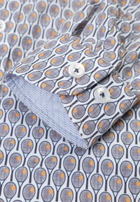 Katoenen shirt met een tennisracketpatroon in marineblauw en oranje op een witte achtergrond. De manchetten hebben een blauw geruit binnenvoering.