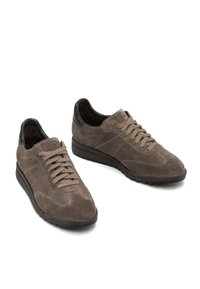 Sneaker in suede marrone con un accento in pelle nera sul tallone, dotate di lacci piatti, punta arrotondata e suola testurizzata.