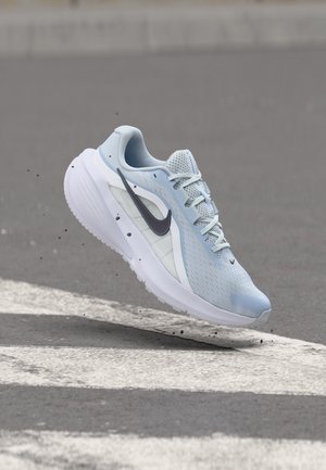 Scarpa da corsa Nike azzurra chiara con suola bianca e logo swoosh nero sembra fluttuare sopra asfalto grigio con segnaletica stradale bianca.