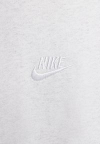 Vit bomullströja med mjuk textur, prydd med en broderad Nike-logga i vit tråd på bröstet.