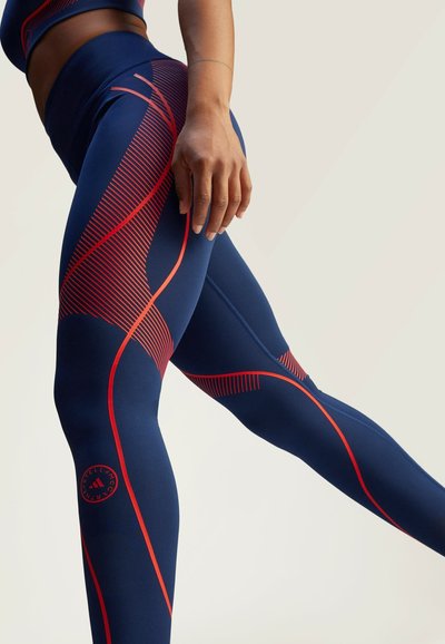 Laivastonsiniset leggingsit, joissa on punaiset vinoviivat ja verkkokuvioita. Sileä, joustava kangas, jossa logo alareunassa. Tiukka istuvuus.