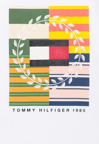 Gráfico multicolorido con formas y franjas superpuestas, que presenta un logo central en rojo y azul marino dentro de una guirnalda de hojas. El texto en la parte inferior dice "Tommy Hilfiger 1985".