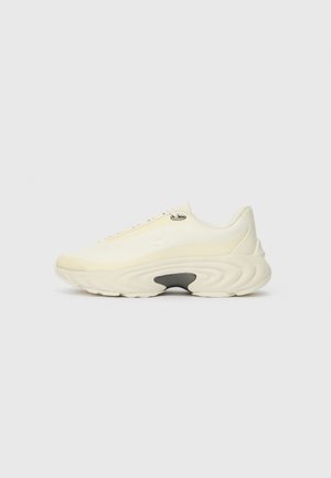 Biały masywny sneaker z grubą podeszwą i subtelnym detalem logo z boku, pokazany z profilu na prostym jasnym tle.