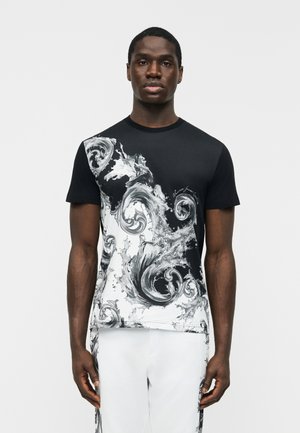 Άνδρας που φοράει μαύρο και άσπρο κοντομάνικο πουκάμισο με κυματιστά λευκά σχέδια και ταιριαστό λευκό παντελόνι με μαύρα σχέδια στις πλευρές.