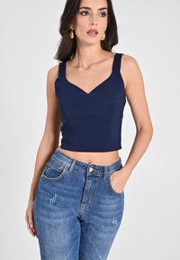 Top corto blu navy con scollatura a V, spalline larghe e una texture liscia, abbinato a jeans in denim azzurro chiaro strappati.