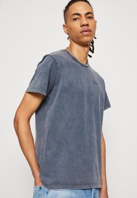 Camiseta de cuello redondo para hombre en azul marino deslavado, de tela de algodón, de manga corta, con un corte relajado y un sutil detalle de logo en el pecho.