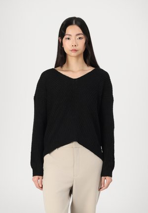 Maglione nero a maglia con scollo a V e texture a costine, caratterizzato da spalle cadenti e orlo curvo. Abbinato a pantaloni color crema.