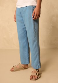Pantalon bleu clair en tissu doux, avec une coupe ample, une forme droite et des poches latérales. Complété par des sandales beige.