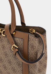Sac à main en toile à motif monogramme marron avec des bords en cuir, une bandoulière réglable, des accessoires en métal doré et deux poignées supérieures.