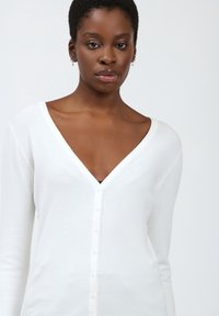 Weißer, langärmeliger Cardigan mit tiefem V-Ausschnitt, der eine Knopfleiste auf der Vorderseite und einen weichen, strukturierten Stoff aufweist.