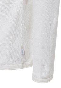 Maglietta a maniche lunghe bianca in maglia con un motivo a trama. Caratterizzata da un orlo arrotondato e una piccola etichetta sulla cucitura laterale. Tessuto morbido.