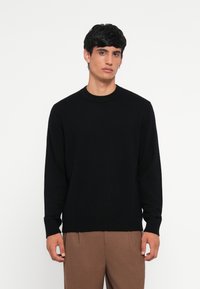 Black knitted sweater with a round neckline, long sleeves, and ribbed cuffs. Textured fabric with a fitted silhouette.