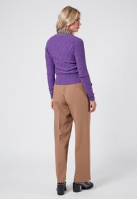 Lila stickad tröja med ett diamantmönster, i kombination med beige vida byxor och kraftiga svarta klackar. Texturerad krage ger extra detalj.