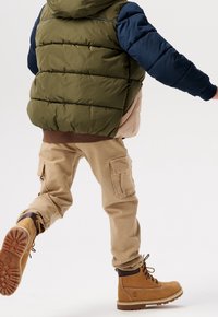 Lunt grøn og blå hættejakke med beige front, brune cargo-bukser og brune snørede støvler med tekstureret sål.