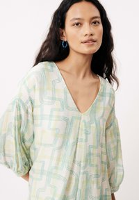 Vloeiende katoenen blouse met V-hals, lichte stof, met een geometrisch patroon in pastelgroen en geel, en puffed mouwen.