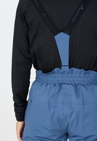 Blauwe buitenbroek met een elastische tailleband en verstelbare banden. Het materiaal lijkt lichtgewicht en duurzaam, met een gladde textuur.