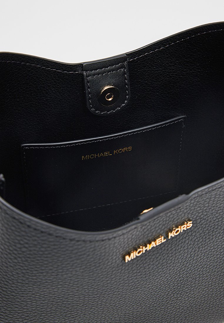 Schwarze Lederhandtasche mit Innenseite, die eine glatte Oberfläche, goldene Beschläge und ein geprägtes Logo auf einer Tasche aufweist. Offenes Design.