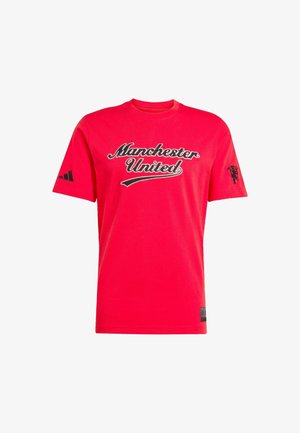 T-shirt en coton rouge avec le texte "Manchester United" en noir, logo Adidas noir sur une manche et logo de lion sur l'autre.