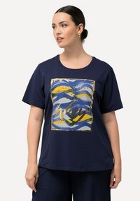 Camiseta de algodón azul marino con un gran estampado gráfico acentuado en dorado que presenta olas abstractas y el texto "SAL DE TU PROPIO CAMINO."