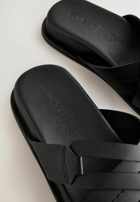 Schwarze Slides-Sandalen aus glattem Material mit konturiertem Fußbett, ausgestattet mit überkreuzten Riemen und eingeprägtem Markenlogo.