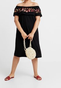Czarna sukienka bez ramiączek z kwiatowym haftem, lekki materiał i luźny krój. Połączona z plecioną torebką i czerwonymi klapkami.