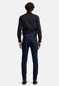 Mörkblå denimjeans med slim fit, försedd med en brun läderlapp och bakfickor med kontrasterande stygn, i kombination med en svart skjorta.