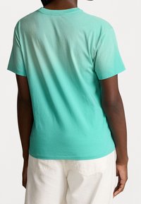 Krátký rukáv bavlněné tričko v gradientu od světle zelené po tmavě zelenou, s kulatým výstřihem a uvolněným střihem, spárované s bílými kalhotami.