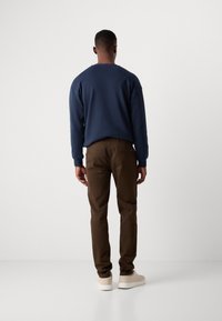 Navy sweatshirt with long sleeves paired with brown pants. The outfit is complemented by beige sneakers. Fabric appears smooth, with a relaxed fit.
