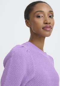 Lavendelfarbener Strickpullover mit einer strukturierten Waffeloptik. Verfügt über einen abgerundeten Ausschnitt und leicht aufgebauschte Ärmel.