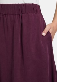 Jupe bourgogne avec une taille élastique et des poches latérales, présentant un tissu texturé et un design fluide.