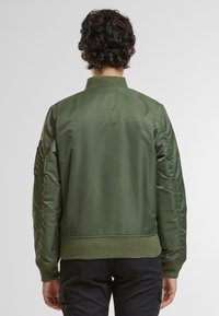 Zelená bomber bunda z hladkej tkaniny s rebrovaným golierom a manžetami. Obsahuje polstrované rukávy a priliehavý lem.