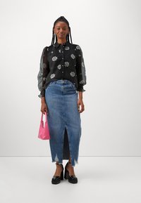 Bluză neagră cu mâneci lungi, brodată cu motive florale și nasturi, asortată cu o fustă din denim cu talie înaltă, având o fanta frontală și margini desfăcute. Ține o geantă roz.