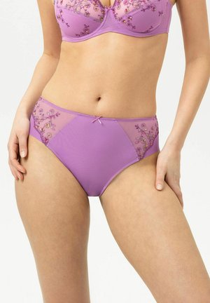 Femme portant un soutien-gorge brodé floral violet et une culotte taille haute assortie, debout sur un fond blanc.