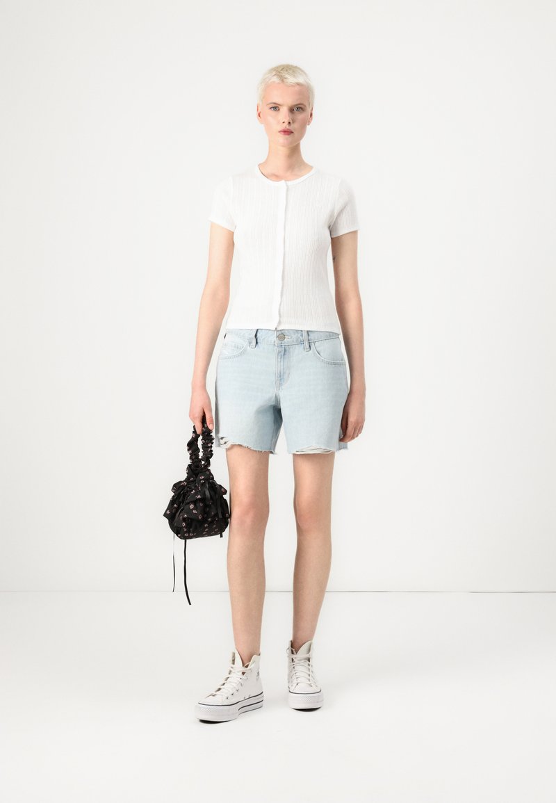 Biały, prążkowany top z krótkim rękawem, jasnoniebieskie szorty dżinsowe z postrzępionym dołem, czarna torba na sznurku w kwiaty oraz białe trampki za kostkę.