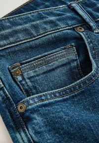 Modré denimové džínsy s vyblednutou textúrou. Medzi vlastnosti patrí malá predná vrecko, zlatý hardware a viditeľné detaily šitia.