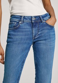 Vaqueros de denim azul con corte recto, diseño de cinco bolsillos, pasadores para cinturón y un ligero desgaste. Cierre de botón y cremallera en la parte delantera.