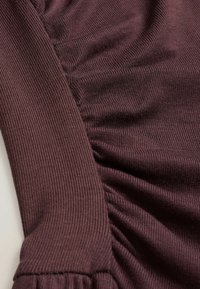 Close-up of a dark purple ribbed fabric with gathered, ruched detailing on one side, highlighting texture and stitching.