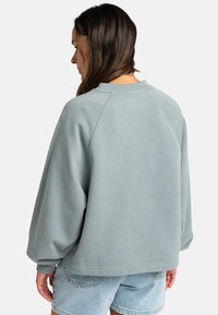 Světlomodrý, nadměrný svetr s raglánovým designem, ribbovaným límcem a manžetami, vyrobený z měkké tkaniny s minimalistickými švy.
