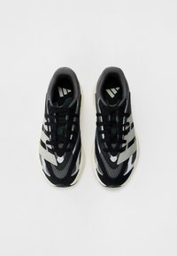 Baskets de sport noires et grises avec une texture en maille et en daim, arborant des rayures blanches contrastantes et des lacets noirs sur le dessus.