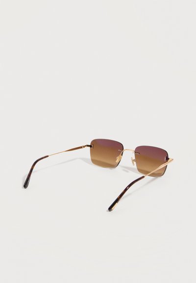 Square-shaped sunglasses with brown gradient lenses and thin gold metal frames laid flat on a white surface.